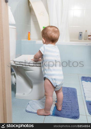 Cute toddler boy standing at bathroom and playing with toilet