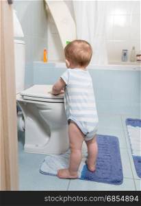 Cute toddler boy standing at bathroom and playing with toilet