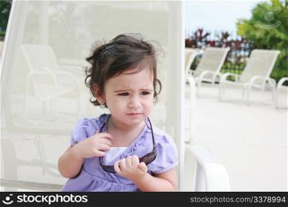 cute toddler girl in summer clothes and sunglasses lyiing on a lounge and relaxing in tropic ocean background