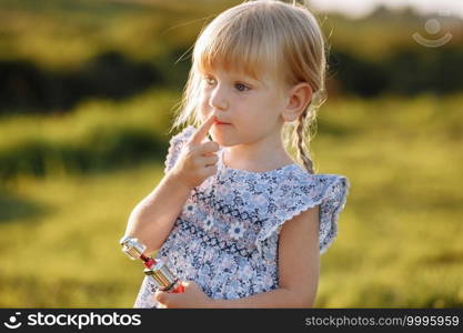 Cute toddler girl rouge her lips with a mother’s lipstick outdoors. Growing up, leadership, copying female psychology behavior concept. Cute toddler girl rouge her lips with a mother’s lipstick outdoors. Growing up, leadership, copying female psychology behavior concept.