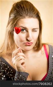 Cute woman holding decorative red heart and looking at camera