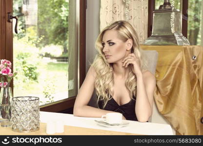 cute woman in black with curly hair style sitting at the table of an elegant old fashion cafe,looking outside