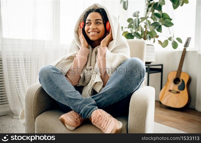 Cute woman in headphones listen to music, guitar on background. Pretty lady in earphones relax in the room, female sound lover resting. Woman listen to music, guitar on background