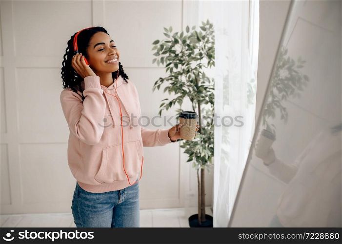 Cute woman in headphones listening to music and drinks coffee. Pretty lady in earphones relax in the room, female sound lover resting. Woman listening to music and drinks coffee