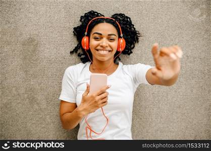 Cute woman in headphones lying on the floor and listen to music, top view. Pretty lady in earphones relax in the room, female sound lover resting. Woman lying on the floor and listen to music