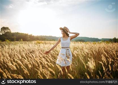 Cute woman in white dress and straw hat harvests wheat in the field. Pretty girl on summer meadow. Cute woman harvests wheat in the field