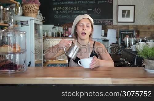 Cute woman pouring milk from a jug into a cup of freshly brewed coffee on the counter in a cafe