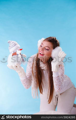 Cute woman with little snowman. Winter fashion.. Pretty cute woman holding little snowman. Attractive girl in earmuffs and white sweater pullover in studio on blue. Winter fashion.