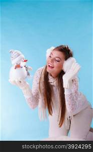 Cute woman with little snowman. Winter fashion.. Pretty cute woman holding little snowman. Attractive girl in earmuffs and white sweater pullover in studio on blue. Winter fashion.
