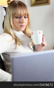 cute young blonde having coffee while working on laptop