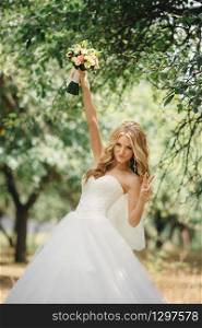 Cute young bride with long hairs holding her wedding bouquet includes white roses and other flowers. Beautiful white marriage dress. Pretty girl on green trees background. Cute young bride with long hairs holding her wedding bouquet includes white roses and other flowers. Beautiful white marriage dress. Pretty girl on green trees background.