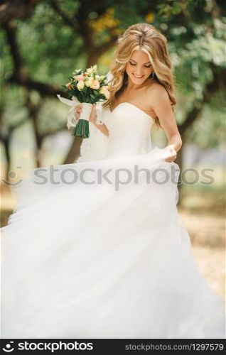 Cute young bride with long hairs holding her wedding bouquet includes white roses and other flowers. Beautiful white marriage dress. Pretty girl on green trees background.. Cute young bride with long hairs holding her wedding bouquet includes white roses and other flowers. Beautiful white marriage dress. Pretty girl on green trees background