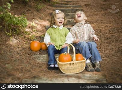 Cute Young Brother and Sister Children Sitting on Wood Steps Laughing with Pumpkins in a Basket.