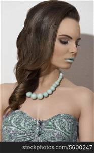 cute young brunette lady posing in close-up fashion shoot with cute smooth elegant hair-style, make-up and green necklace