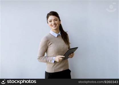 Cute young business woman standing by the white office wall and using digital tablet