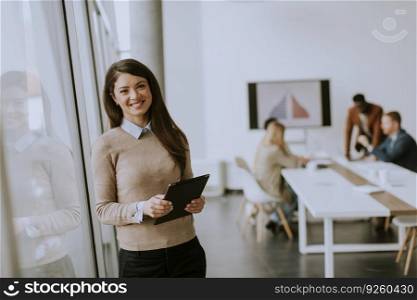 Cute young business woman standing in the office and using digital tablet in front of her team