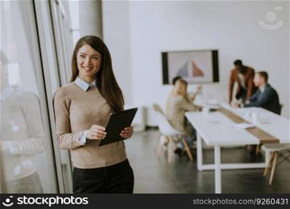 Cute young business woman standing in the office and using digital tablet in front of her team