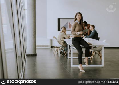 Cute young business woman standing in the office and using digital tablet in front of her team