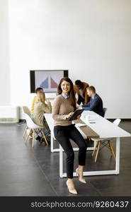 Cute young business woman standing in the office and using digital tablet in front of her team