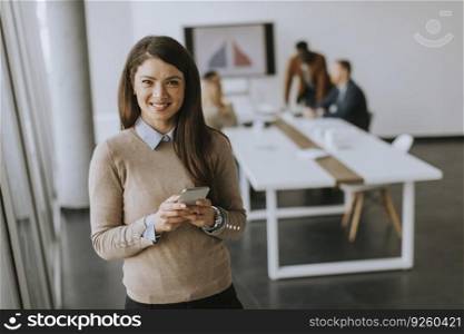Cute young business woman standing in the office and using mobile phone in front of her team