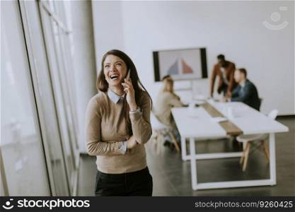 Cute young business woman standing in the office and using mobile phone in front of her team