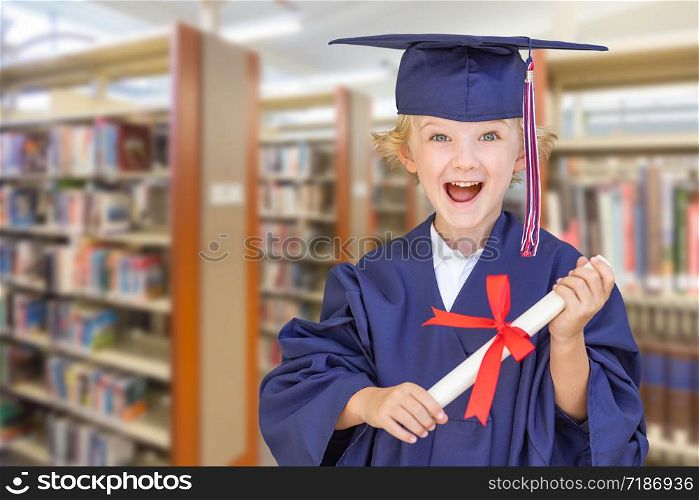 Cute Young Caucasian Boy Wearing Graduation Cap and Gown in The Library.