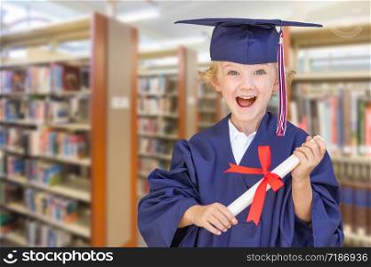 Cute Young Caucasian Boy Wearing Graduation Cap and Gown in The Library.