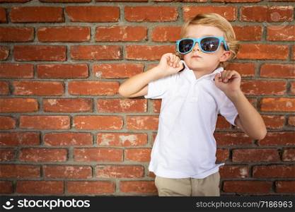 Cute Young Caucasian Boy Wearing Sunglasses Against Brick Wall.