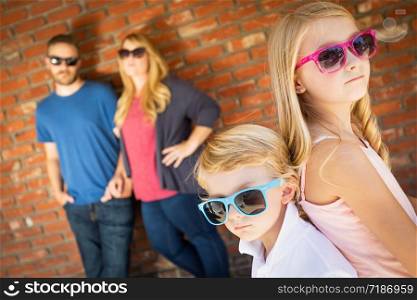 Cute Young Caucasian Brother And Sister Wearing Sunglasses with Parents Behind.
