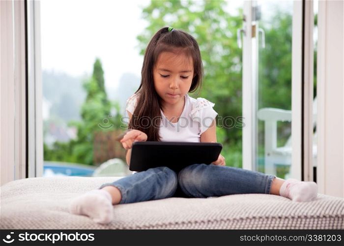 Cute young child using a digital tablet in a home interior with large window