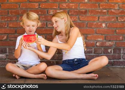 Cute Young Cuacasian Boy and Girl Eating Watermelon Against Brick Wall.
