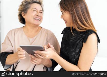 Cute young daughter teaching her happy old elderly mother to use digital tablet at home
