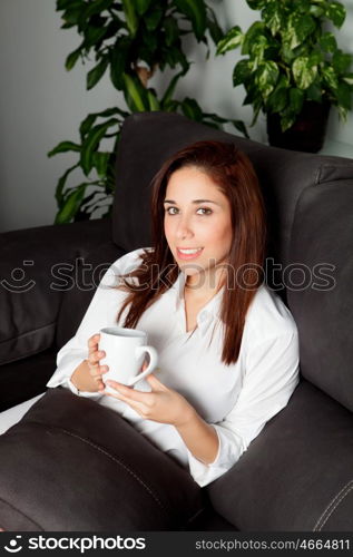 Cute young drinking a hot cup of tea sitting on the couch at home