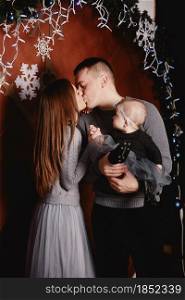cute young family dad, mom and baby daughter are hugging and kissing on Christmas background. Merry Christmas and Happy New Year holidays.. cute young family dad, mom and baby daughter are hugging and kissing on Christmas background. Merry Christmas and Happy New Year holidays
