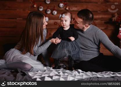 cute young family on bed with Christmas background behind. mom, dad and baby girl enjoy time together.. cute young family on bed with Christmas background behind. mom, dad and baby girl enjoy time together