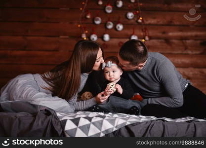 cute young family on bed with Christmas background behind. mom, dad and baby girl enjoy time together.. cute young family on bed with Christmas background behind. mom, dad and baby girl enjoy time together