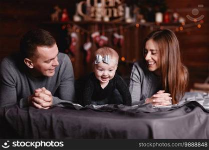 cute young family with dad, mom and baby girl on bed with Christmas background behind. cute young family with dad, mom and baby girl on bed with Christmas background behind.