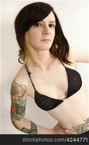 Cute young female looking into the camera with arm tattoos and wearing black bra.