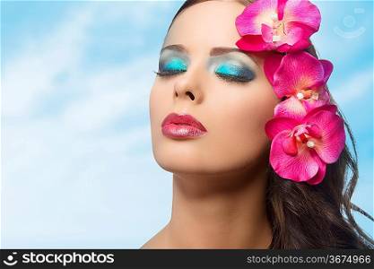 cute young girl in a beauty portrait with coloured make-up and pink flowers against sky . FAKE FLOWERS