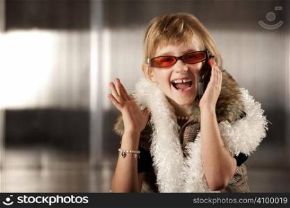 Cute young girl in dress-up clothes and red sunglasses talking on cell phone