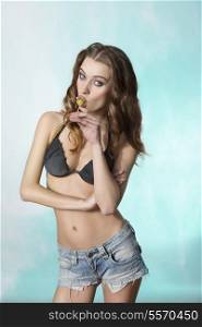 cute young girl posing with summer style and long natural hair, wearing bikini and shorts and eating lollipop