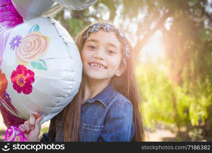 Cute Young Mixed Race Girl Holding Mylar Balloon Outdoors.