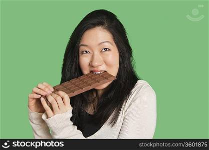 Cute young woman eating a large chocolate bar over green background