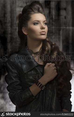 cute young woman posing in fashion portrait with modern leather jacket, rock accessories, long wavy hair-style. Dark look