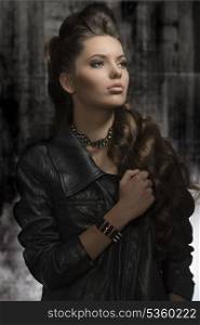 cute young woman posing in fashion portrait with modern leather jacket, rock accessories, long wavy hair-style. Dark look