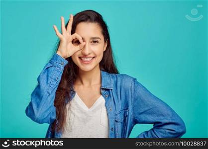 Cute young woman shows ok dign, blue background, positive emotion. Face expression, female person looking on camera in studio, emotional concept, feelings. Cute young woman shows ok dign, positive emotion