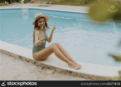 Cute young woman sitting by the swimming pool and taking selfie photo with  mobile phone in the house backyard
