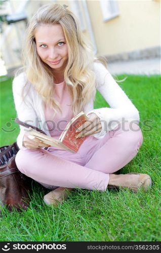 Cute young woman sitting on the grass and reading the book