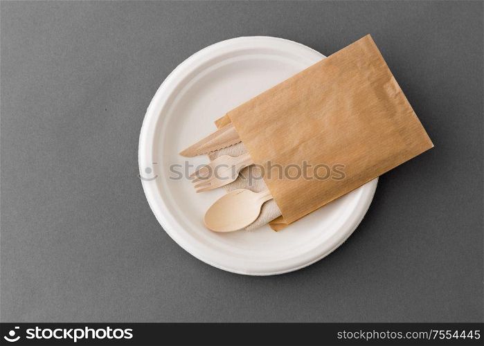 cutlery, recycling and eco friendly concept - set of wooden spoon, fork and knife on paper plate on grey background. wooden spoon, fork and knife on paper plate