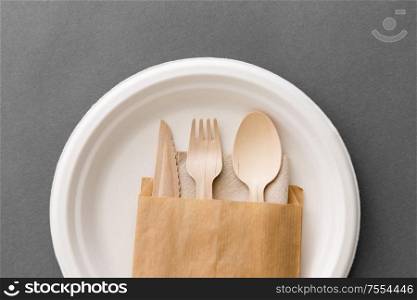 cutlery, recycling and eco friendly concept - set of wooden spoon, fork and knife on paper plate on grey background. wooden spoon, fork and knife on paper plate